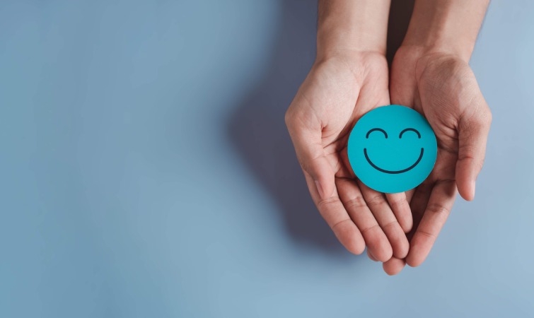 Manos sosteniendo un círculo azul con una cara sonriente sobre fondo azul