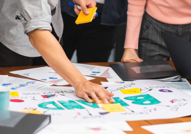 Un equipo de marketing trabaja reunido en una mesa con notas adhesivas, gráficos y un cartel de estrategia de marca