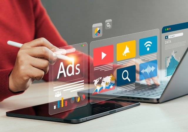 Una persona gestiona campañas de publicidad digital e inbound marketing a través de gráficos flotantes interactivos, un ordenador portátil y una tableta